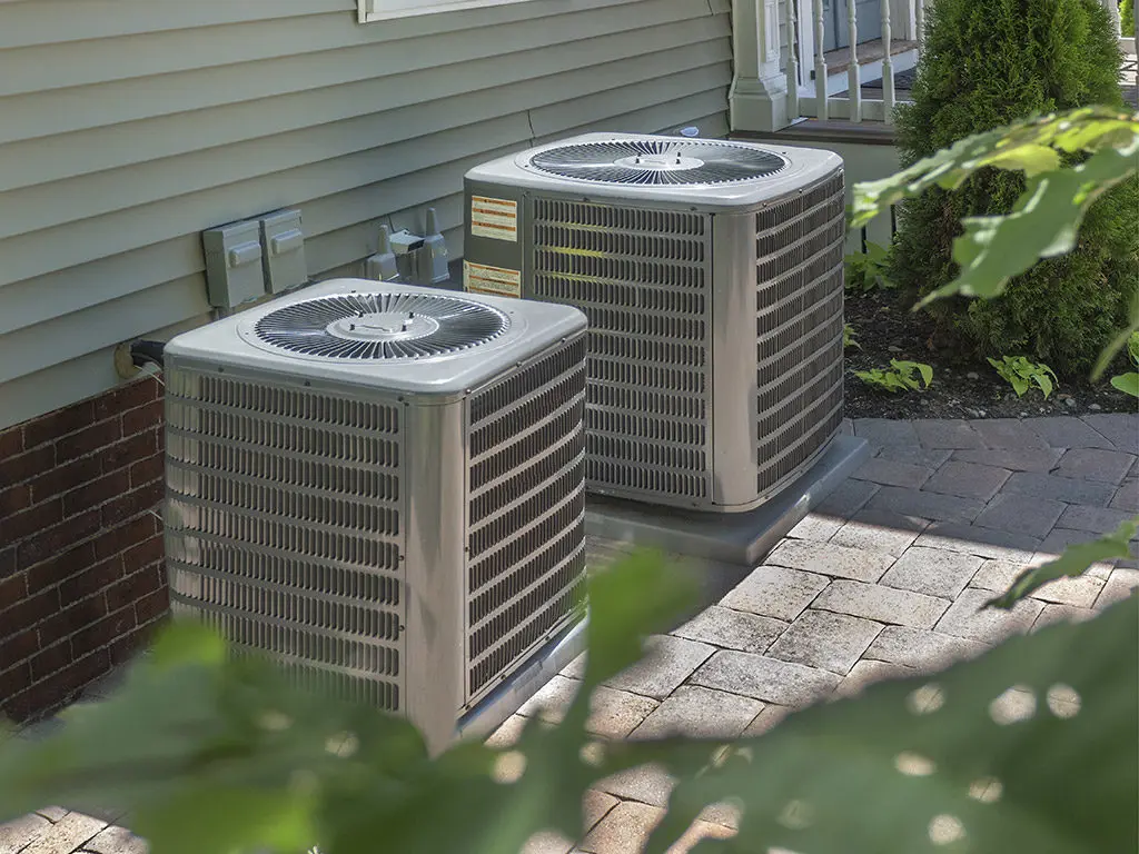 Two air conditioners are sitting outside of a house.